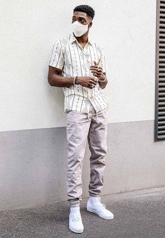 Tenue: Chemise à manches courtes imprimée blanche et noire, Pantalon chino beige, Baskets basses en toile blanches, Montre argentée