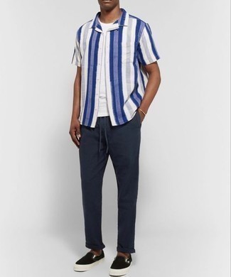 Tenue: Chemise à manches courtes à rayures verticales blanc et bleu marine, T-shirt à col rond blanc, Pantalon chino bleu marine, Baskets à enfiler en toile noires
