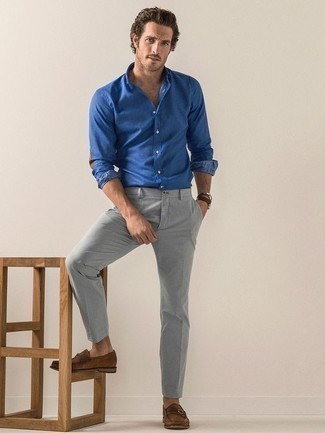 Tenue: Chemise à manches longues en chambray bleue, Pantalon chino gris, Slippers en daim marron, Montre en cuir marron foncé